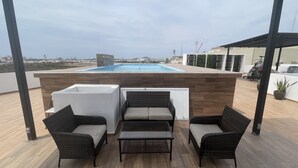 A rooftop terrace with a pool, outdoor seating, and a view of the cityscape. - Departamento con alberca en El Encanto (Mazatlán)
