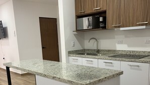 A modern kitchen with a central island, white cabinetry, and a wooden upper shelf. - Departamento con alberca en El Encanto (Mazatlán)