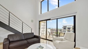 Ein modernes Wohnzimmer mit einem braunen Ledersofa, einem weißen Sessel und einem runden Couchtisch. Ein großes Fenster bietet Blick ins Freie.