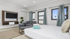 A modern hotel room with a large bed, a sofa, a TV mounted on the wall, and a window with curtains. - *NEW* 4BR4BA Villa across of PalmBeach w/ Pvt Pool (Noord)