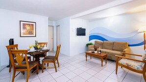 A living room with a dining table, chairs, a sofa, and a TV mounted on the wall. - Quiet, Cozy & Central ~ Close to the Beach ~ Pool! (Noord)
