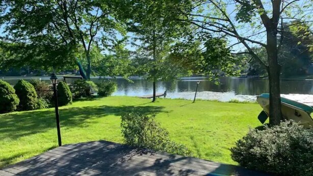 A deck with a view of a lake, surrounded by greenery and trees. - Beautiful 3 Bedroom Lakefront Home (Sweet Valley)