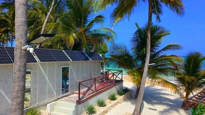 Un bâtiment situé en bord de mer, doté de panneaux solaires, d’une rambarde rouge et de palmiers.
