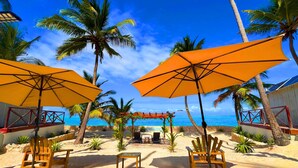 Un espace aménagé avec des chaises en bois et des parasols orange, situé en bord de plage et offrant une vue sur une mer d’un bleu limpide.
