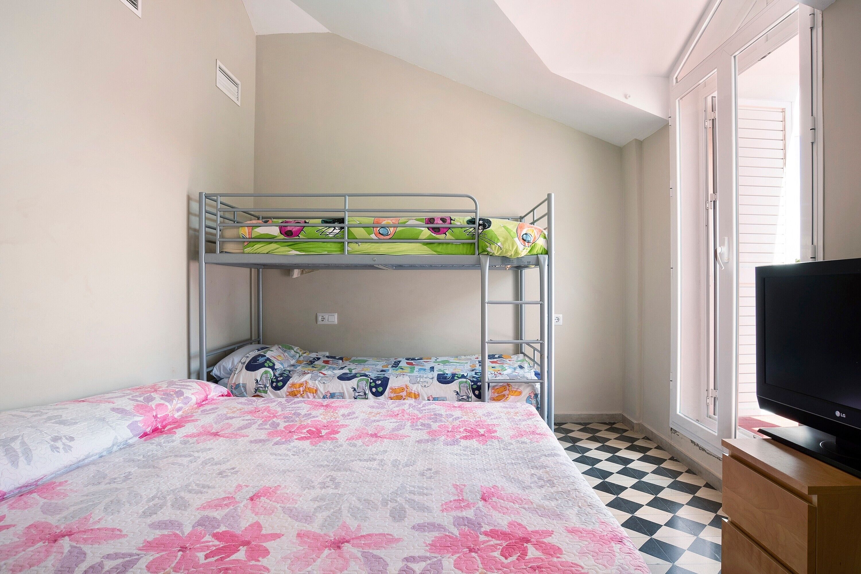 Una cama litera con ropa de cama floral, un televisor sobre un soporte de madera y un piso a cuadros.