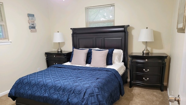 A bedroom with a dark wooden bed, two bedside tables with lamps, a beige carpet, and a wall with a motivational quote. - Stock Cottage Cozy 2 BR, 2 Bath House next to Biology Trails and SAU (Ooltewah)