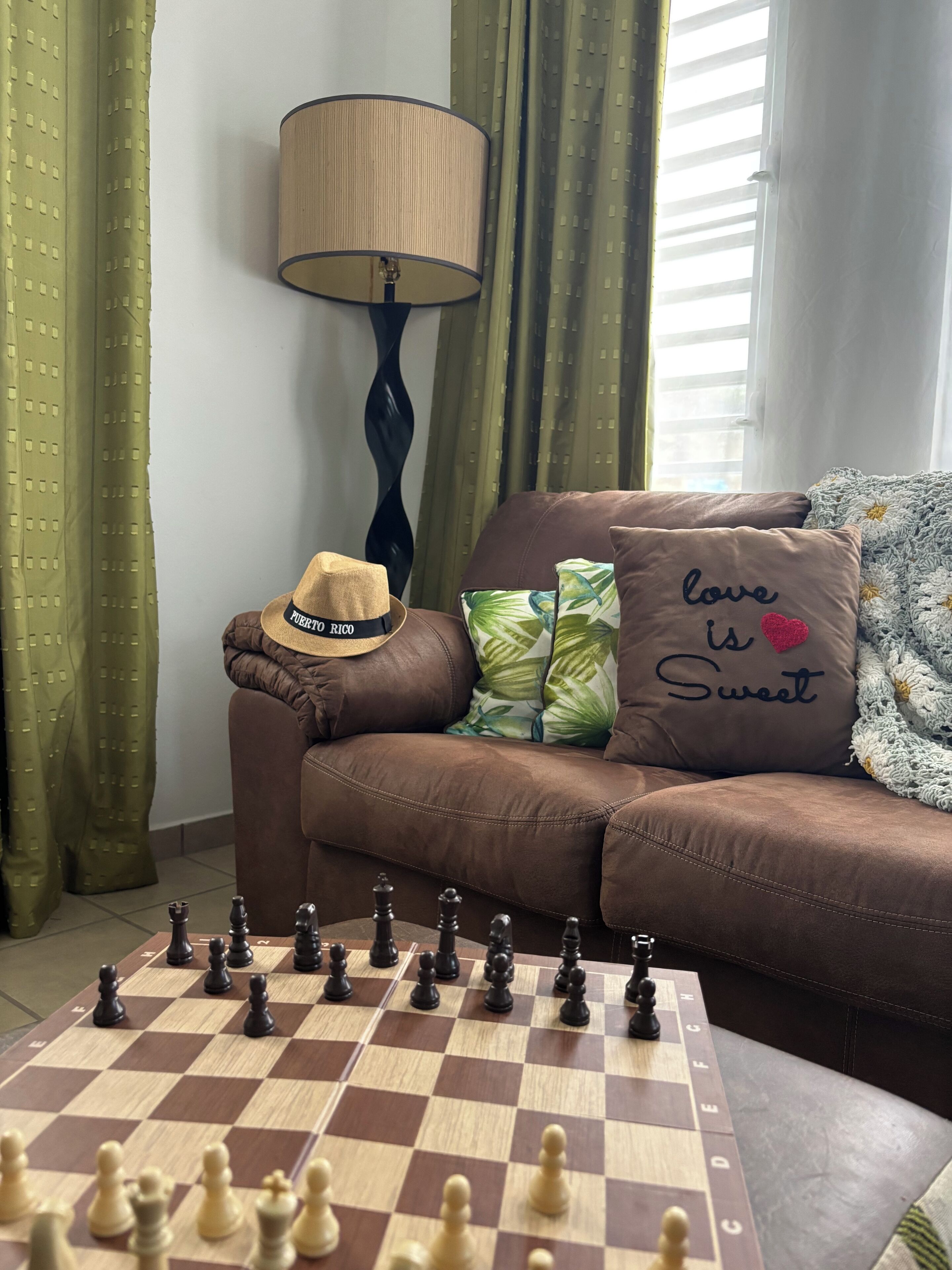 Ein Wohnzimmer mit Schachbrett, einer Couch, einem Hut und einer Lampe.