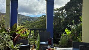 An outdoor patio with wicker furniture, a table with a plate of food, and potted plants. - Rainforest Escape with Stunning Views minute's drive away from everything! (Río Grande)