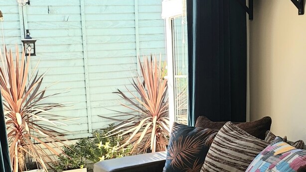 A cozy room with a sofa, a window with curtains, and a view of a green building outside.