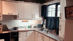 A kitchen with white cabinets, a black countertop, and a window with blinds.