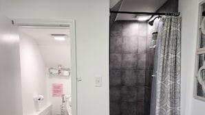 Baño con ducha, inodoro y lavamanos. Incluye un perchero y un cubo de basura.
