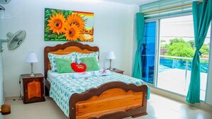 A bedroom with a wooden bed, two bedside tables with lamps, a large window with curtains, and a painting of sunflowers.