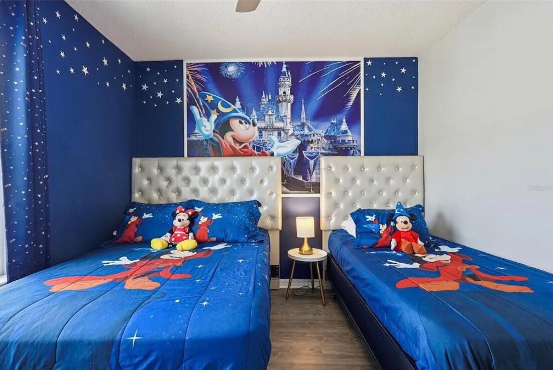 A room with two beds, each with a Mickey Mouse themed bedspread. There is a wall mural of a castle and fireworks.