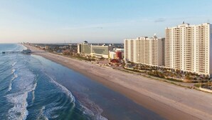 A coastal hotel with multiple high-rise buildings, a beach, and a pier.