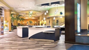 A hotel reception area with a central counter, multiple seating areas, and a decorative ceiling with hanging lights.