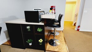 Un petit espace cuisine comprenant un plan de travail, un réfrigérateur noir et un évier. Quatre plantes en pot sont disposées sur un meuble situé sous le plan de travail.