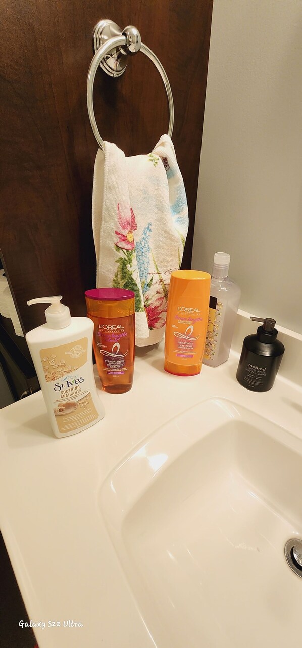 A bathroom sink with various toiletries including a bottle of L'Oreal hair care product, a bottle of Method body wash, and a bottle of St. Ives body lotion. - Unique full basement suite with spacious living room. (Airdrie)
