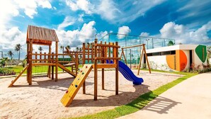 Un parque infantil con tobogán y estructuras para escalar, rodeado por una valla y palmeras.