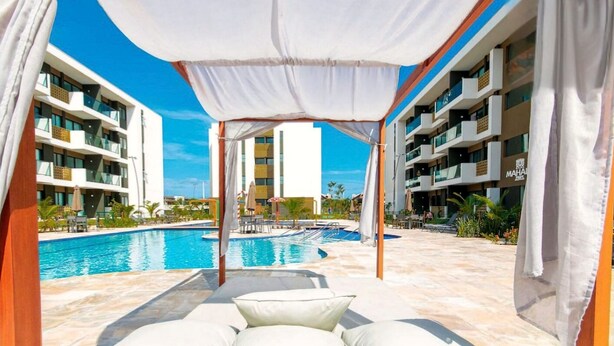 Zona junto a la piscina con una pérgola, sillas de descanso y vista despejada a la piscina.