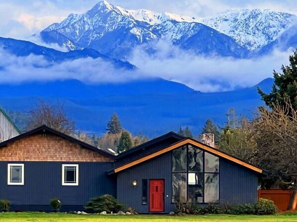 Ein modernes, zweistöckiges Haus mit roter Tür, großen Fenstern und einer Ziegelaußenwand.
