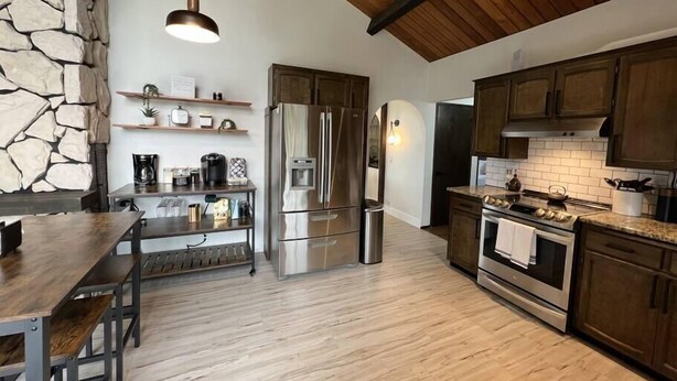 Une cuisine moderne avec des meubles en bois, un réfrigérateur en acier inoxydable et une table à manger en bois, accompagnée de bancs.