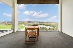 A balcony with a wooden table and chairs, overlooking a residential area and a body of water. - Dream retreat ! Escape, Relax and Rejuvenate. (Berwick)