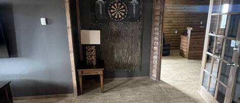 A room with a dartboard, a small table with a lamp, and a wooden floor.