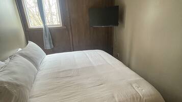 Une chambre avec un plafond en bois, un lit avec une literie blanche, une fenêtre avec des rideaux et un téléviseur à écran plat fixé au mur.