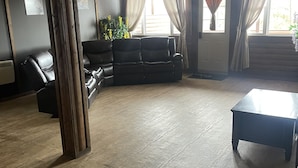 A spacious living room with a dark leather sofa, a wooden coffee table, and a large window with curtains. - Harbour Hutch  (St. Anthony)