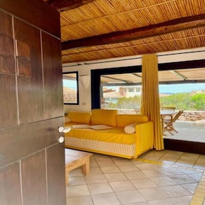 Una habitación con un sofá amarillo, una mesa de madera y vistas al exterior.