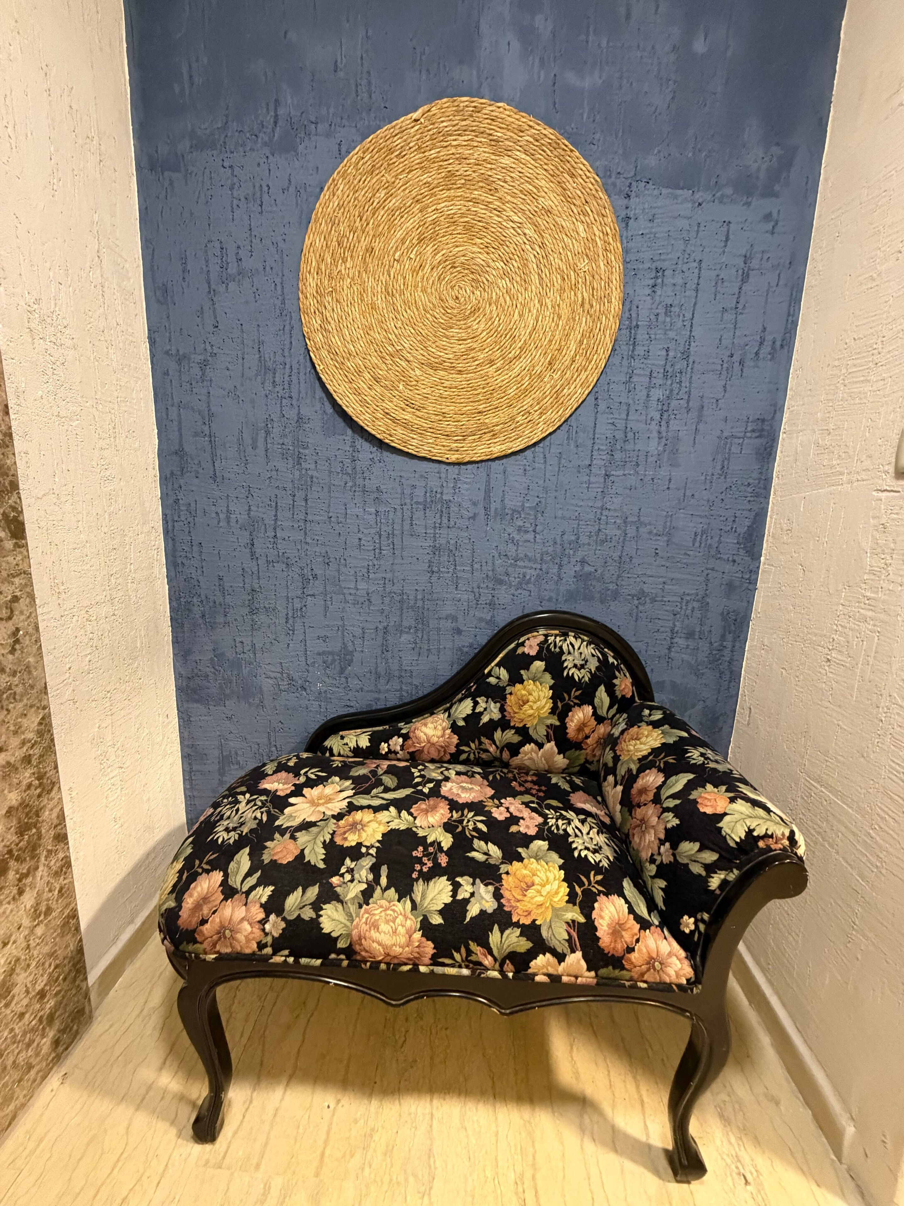 Ein Blick in einen Raum mit blauer Wand, einem gewebten Wandbehang und einer floral gepolsterten Bank.