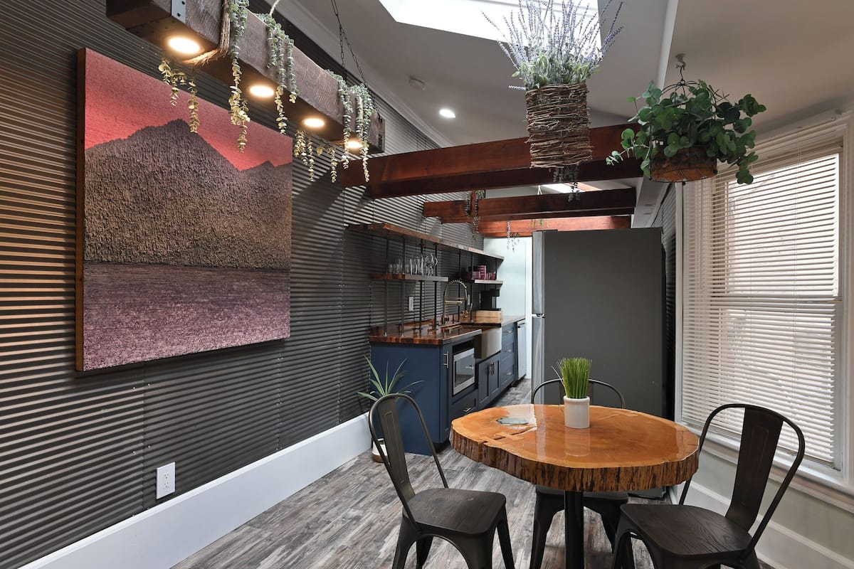 A modern kitchen with dark cabinetry, a wooden island, and hanging plants.