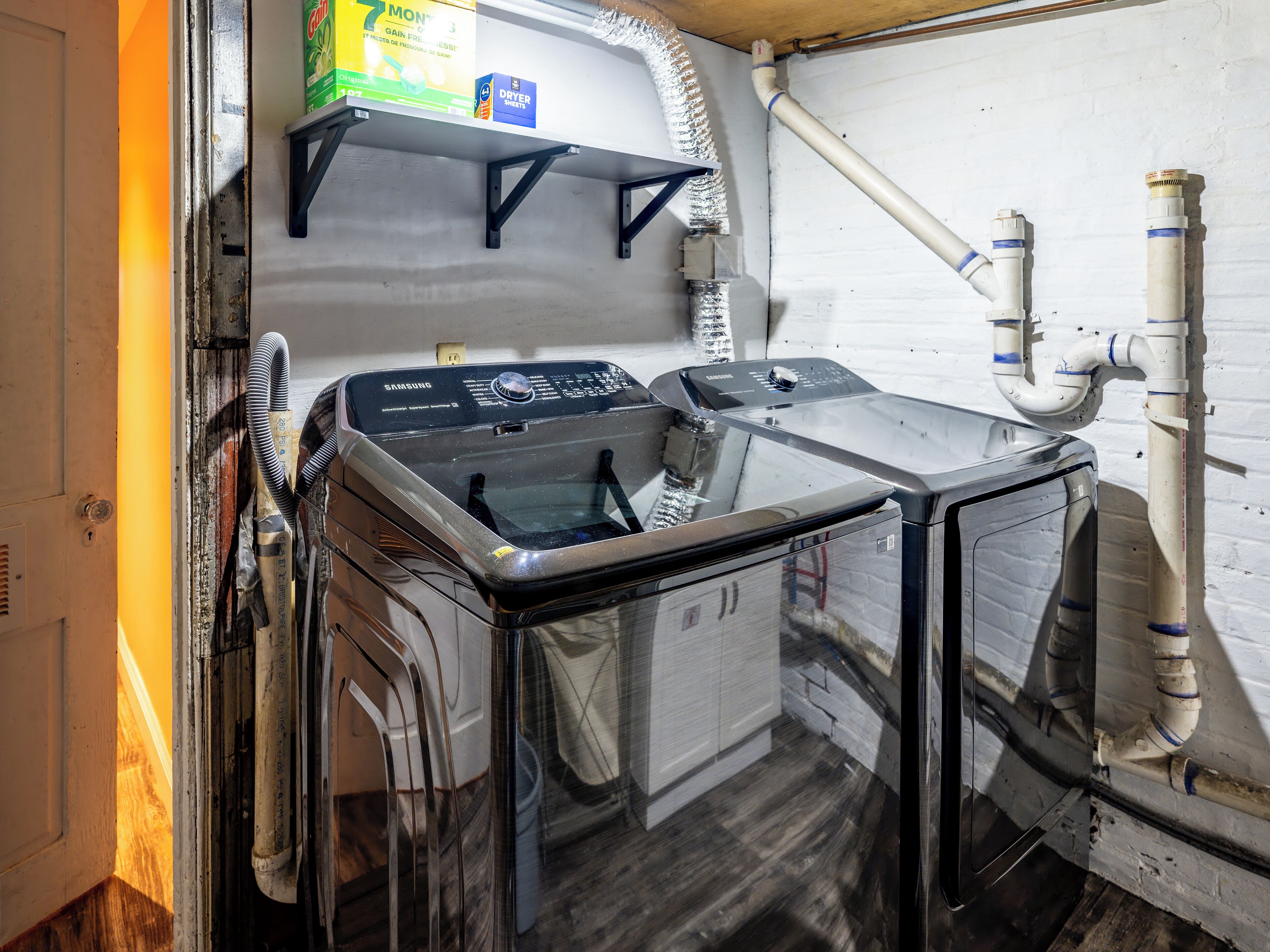 A compact laundry room with a washing machine, dryer, and shelving unit.