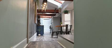 A hallway with wooden beams, a skylight, a dining area with a table and chairs, and a potted plant.
