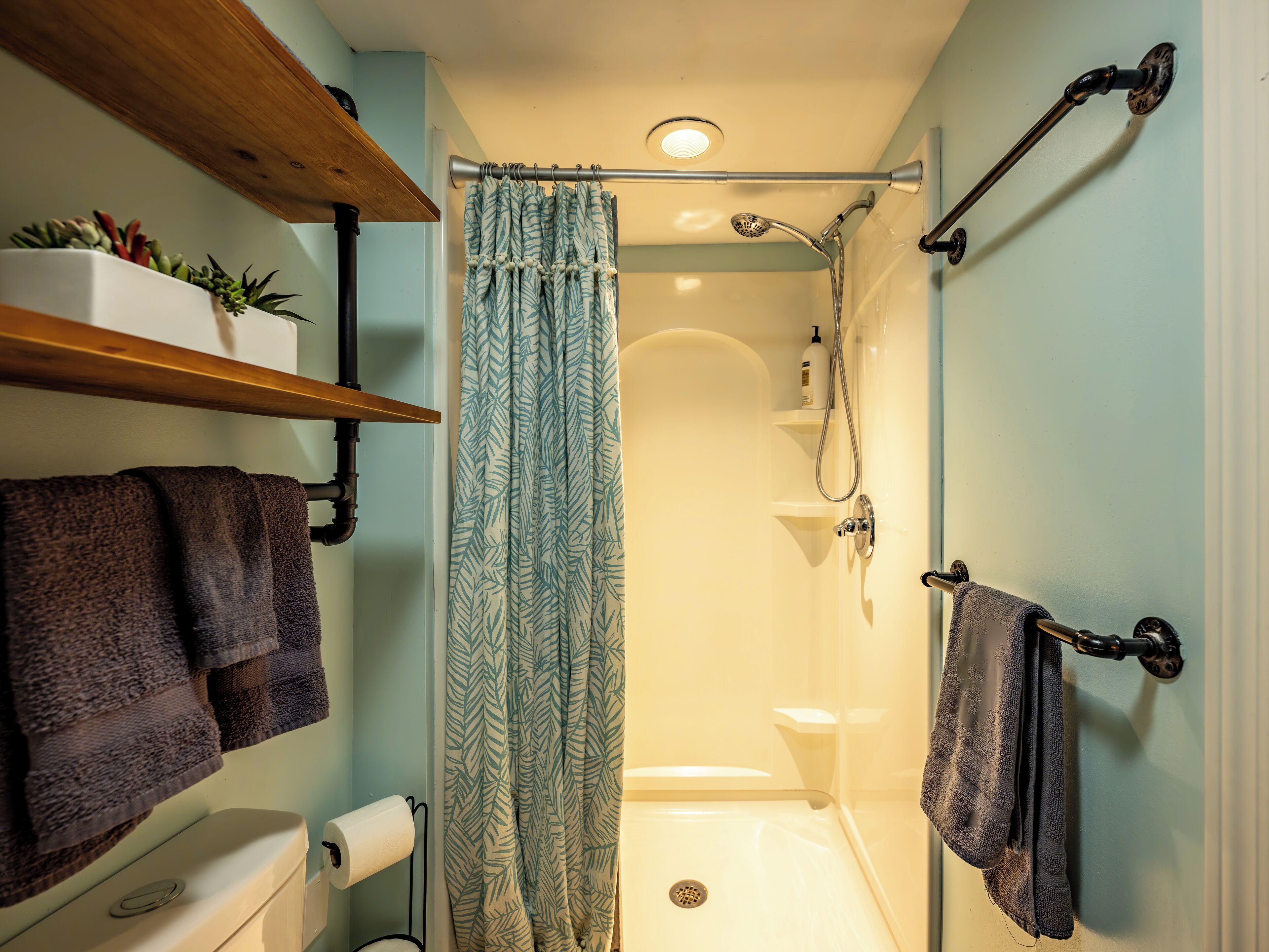 Une salle de bain équipée d’une douche, de toilettes, d’un porte-serviettes et d’une étagère avec des plantes.