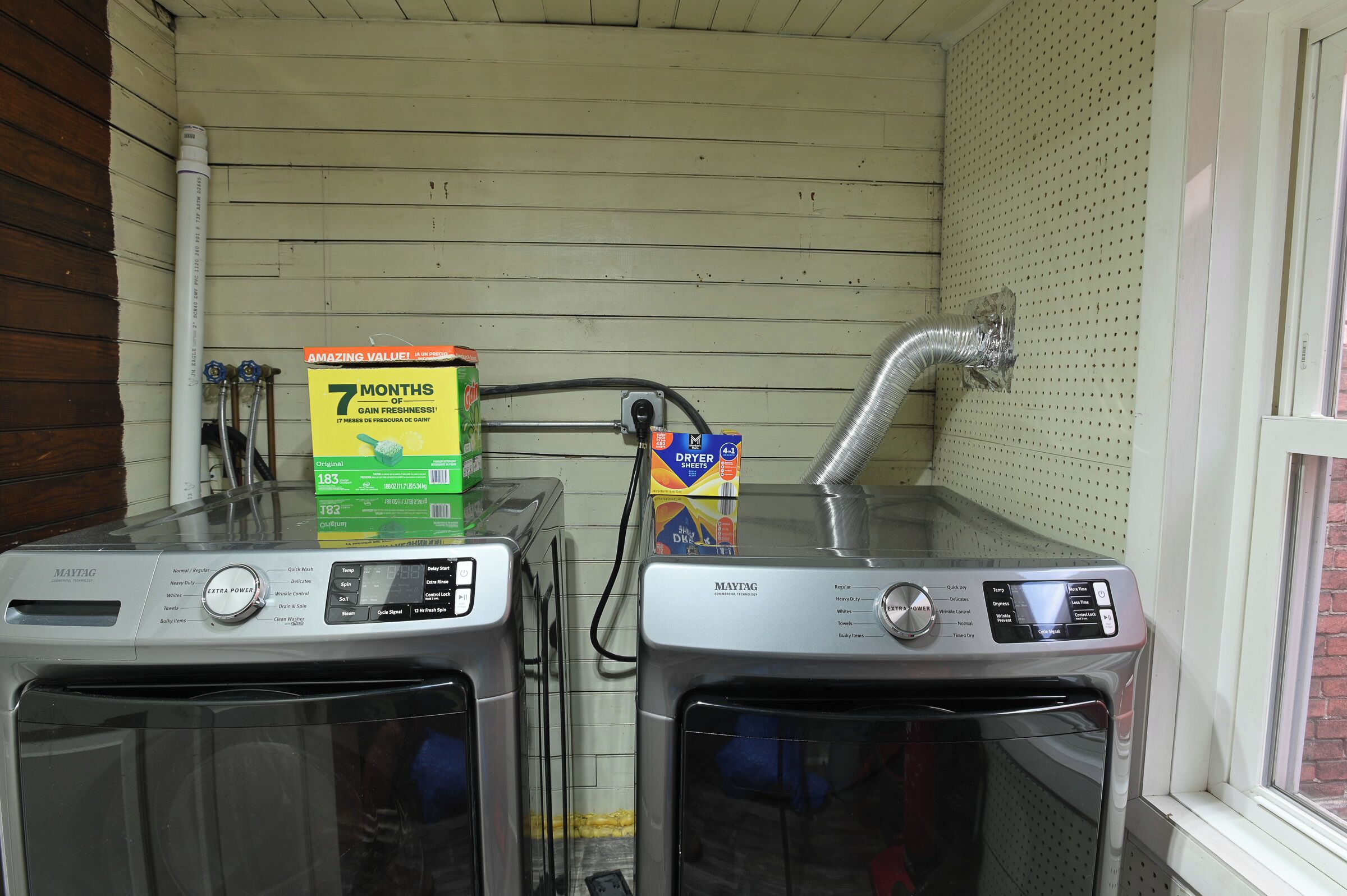 Two front-loading washing machines with control panels, a hose, and a box of dryer sheets on top.