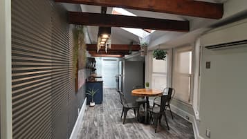 Un pasillo estrecho con una mesa y sillas de madera, una planta en maceta y una planta colgante.