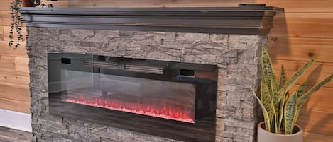 A stone fireplace with a glass front, a mounted television above it, and a potted plant to the right.