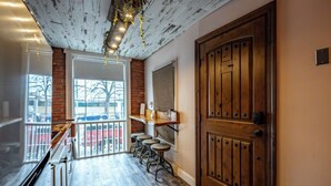 A wooden door with a brass handle, a brick wall, and a window with a view of parked cars outside. - BurgBnB Downtown (Harrisburg)