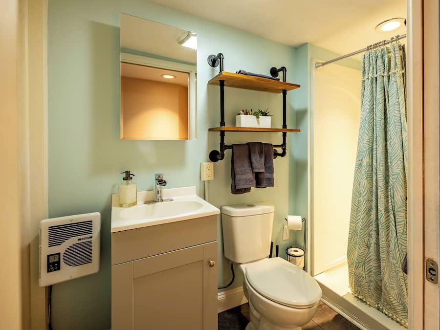 A bathroom with a toilet, sink, mirror, towel rack, shower curtain, and a radiator.