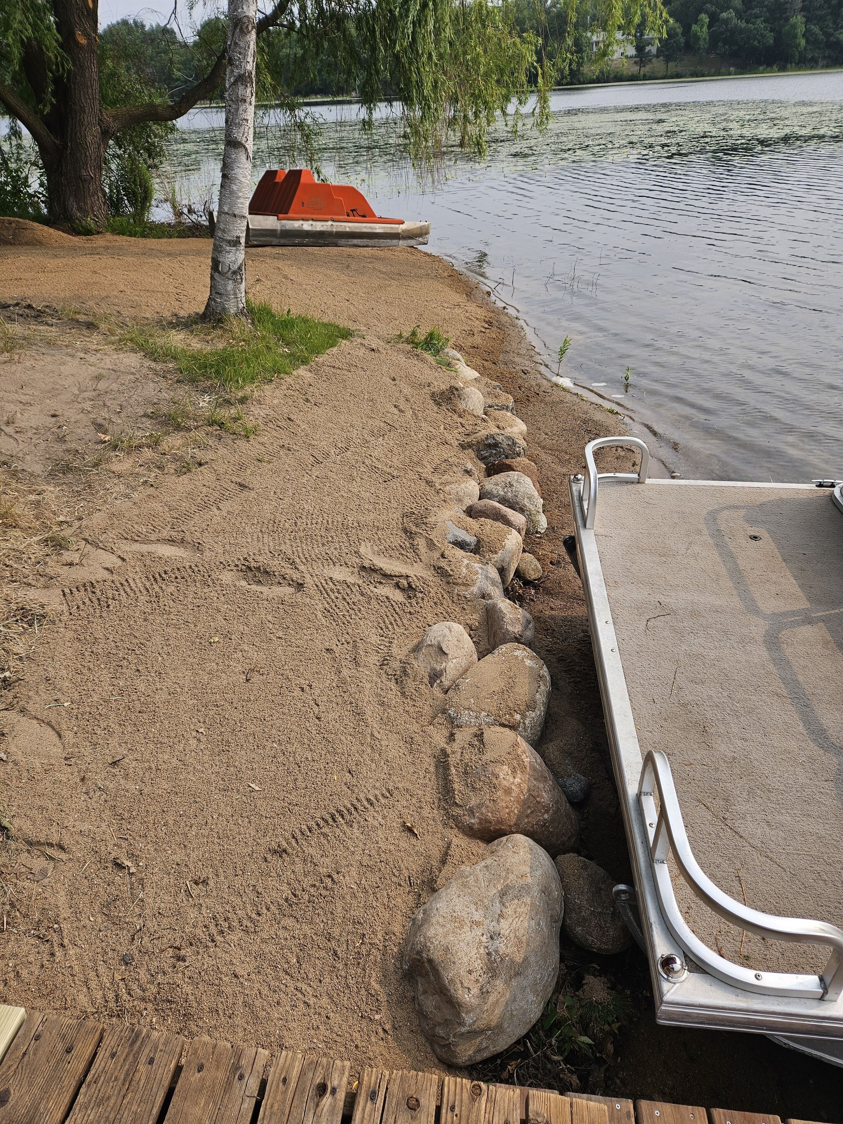 A sandy beach with a row of rocks leading to a dock with a boat.