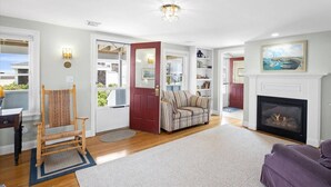 A living room with a fireplace, a sofa, a wooden chair, and a bookshelf. - Oceanfront Family Retreat in Scituate with Private Beach, Expansive Porches, Outdoor Shower (Scituate)