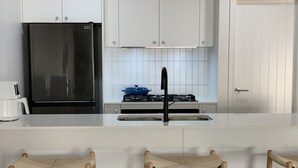 Keittiössä on musta jääkaappi, valkoiset kaapit, kaasuliesi ja kolme puista jakkaraa.