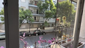 En balkon med blomsterkrukker og udsigt til en gade med biler og bygninger.