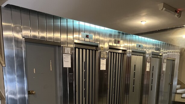 Et moderne elevatorområde med metaldøre og et gulv med marmorlook.