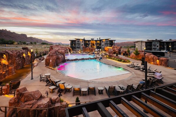 Relax by the central pool surrounded by lounge chairs and benches, amidst a landscaped area with rock formations and a water feature.