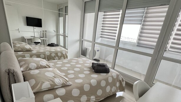 A modern hotel room with a large bed, a desk, and a chair. There is a TV mounted on the wall, and the room has large windows with blinds. - Super 4 Rooms refurbished (Villeurbanne)