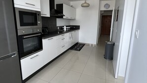 A modern kitchen with white cabinetry, stainless steel appliances, and a black countertop. - Super 4 Rooms refurbished (Villeurbanne)
