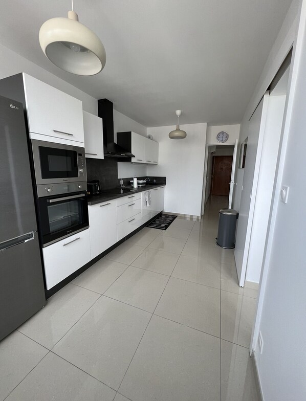 A modern kitchen with white cabinetry, stainless steel appliances, and a black countertop. - Super 4 Rooms refurbished (Villeurbanne)