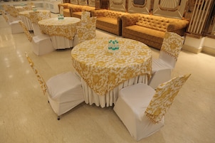 A banquet hall with round tables and white chairs, each covered with a patterned tablecloth.